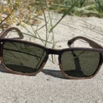 Lunettes de soleil Draken en bois de noyer et ébène avec design carré élégant, posées sur du sable.