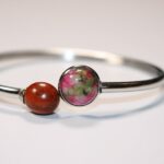 Un bracelet jonc argenté avec un cabochon en bois d'acajou et une pierre de jaspe vert et rose.
