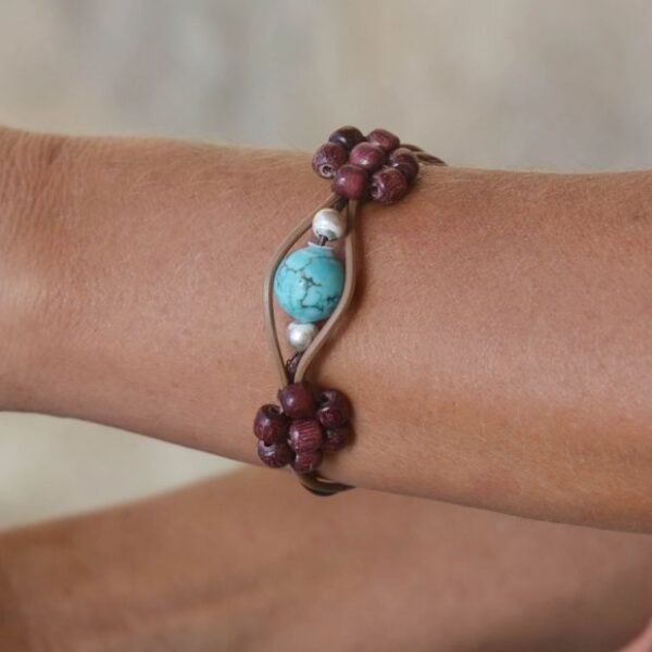 Un bracelet en cuir beige et marron foncé avec une pierre turquoise centrale et des perles en bois d’amarante.