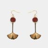 Femme portant les boucles d’oreilles Nancy en feuille ginkgo amarante