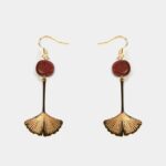 Femme portant les boucles d’oreilles Nancy en feuille ginkgo amarante