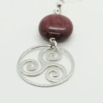 Bijoux en bois d'amarante et filigrane argenté représentant un triskel, présentés sur un fond doux.