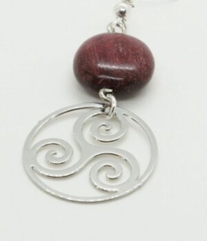 Bijoux en bois d'amarante et filigrane argenté représentant un triskel, présentés sur un fond doux.