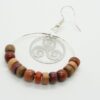 Boucles d’oreilles créoles en bois multicolore et filigrane argenté en forme de triskel, posées sur fond neutre.