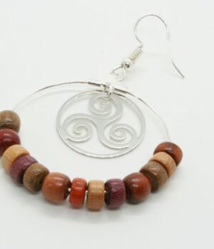 Boucles d’oreilles créoles en bois multicolore et filigrane argenté en forme de triskel, posées sur fond neutre.