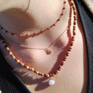 Collier triple Quartz et bois Juliane sur fond blanc, montrant la chaînette en acier inoxydable avec des perles rouges, et la chaîne avec un charme arbre de vie.