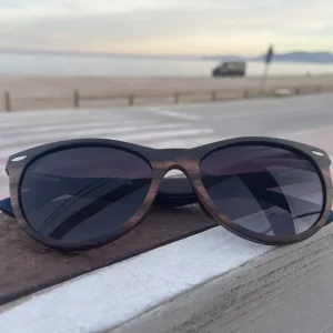 Lunettes de soleil BRIGITTE en bois de palissandre, monture papillon élégante posée sur une surface beige.