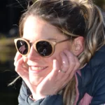 Lunettes de soleil Élizabeth en bois naturel, posées dans leur étui raffiné en liège, entourées d’accessoires minimalistes.