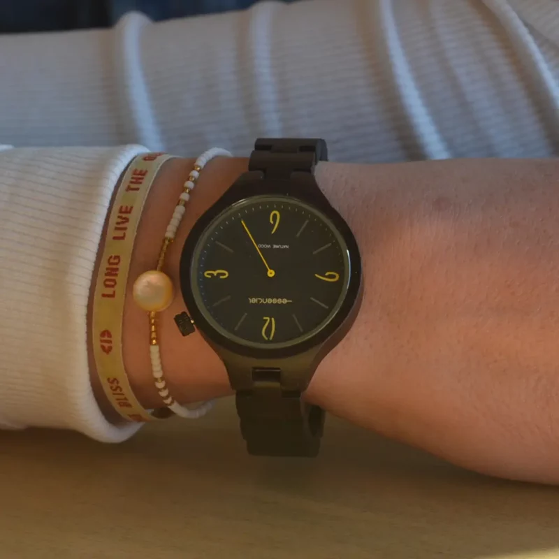 Cadran noir de la montre Aretha en bois d'ébène avec accents jaunes sur les chiffres.