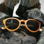 Lunettes de soleil Spector Orange en bois recyclé avec un design multicolore, posées sur une surface marbrée.