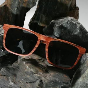 Lunettes rectangulaires en bois de noyer GLOSTER-4 avec des verres gris polarisés, posées sur une table en bois. Un design élégant et éco-responsable pour hommes."