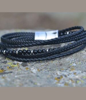 Bracelet multi-rangs en cuir noir tressé avec pierres naturelles en onyx, posé sur un socle en pierres.